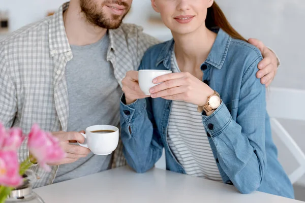 Vista cortada de casal com xícaras de café sentado na cozinha — Fotografia de Stock