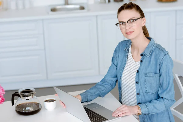 Mulher atraente fazendo trabalho remoto no laptop na cozinha com café — Fotografia de Stock