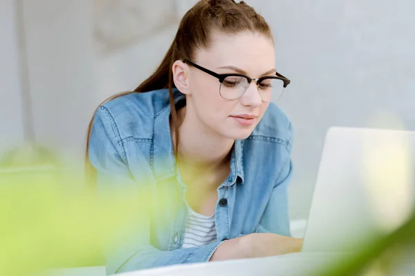 Attrayant jeune femme dans des lunettes en utilisant un ordinateur portable — Photo de stock