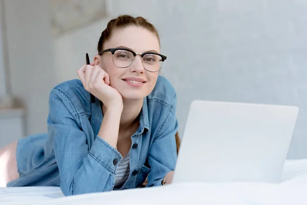 Young smiling female freelancer with laptop on bed — Stock Photo