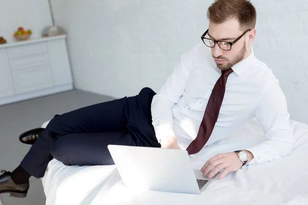 Uomo d'affari in occhiali utilizzando il computer portatile in camera da letto — Foto stock