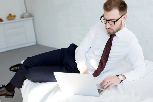 Hombre de negocios en gafas con portátil en el dormitorio - foto de stock