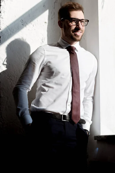 Feliz hombre de negocios en corbata y gafas posando cerca de la pared blanca - foto de stock