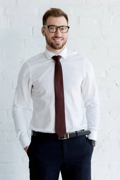 Uomo d'affari sorridente in occhiali posa vicino muro bianco — Foto stock
