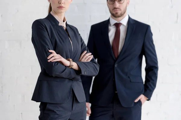 Cropped view of businessman and businesswoman with crossed arms posing near white wall — Stock Photo