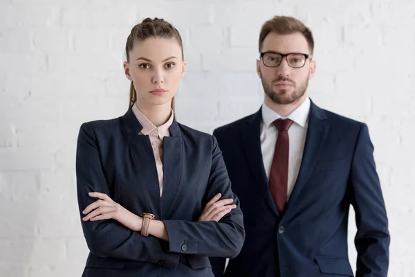 Businessman and businesswoman with crossed arms posing near white wall — Stock Photo