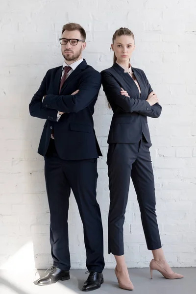 Equipe de negócios profissional em ternos posando com braços cruzados perto da parede branca — Fotografia de Stock