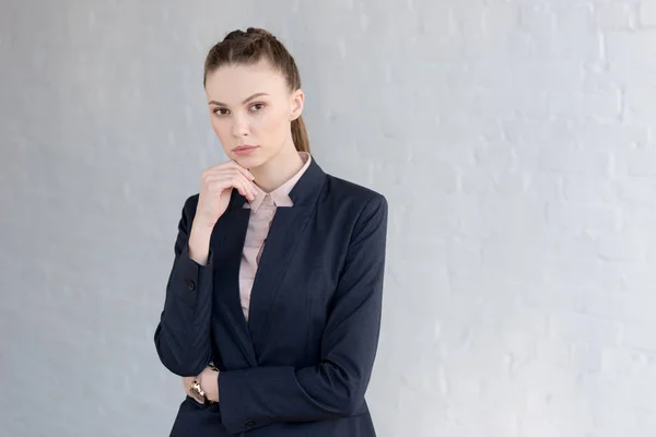 Pensive businesswoman in formal wear posing near white wall — Stock Photo