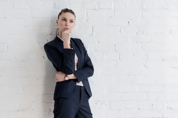 Beautiful thoughtful businesswoman in suit posing near white wall — Stock Photo