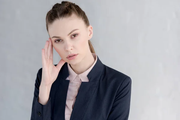 Tired businesswoman in suit with headache standing near white wall — Stock Photo