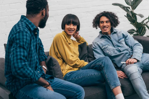 Multicultural smiling friends sitting on couch and talking to each other — Stock Photo