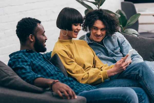 Young mixed race woman showing smartphone screen to male friends — Stock Photo