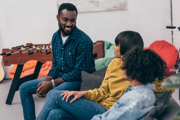 Gruppo di amici multiculturali sorridenti seduti sul divano e che parlano tra loro — Foto stock