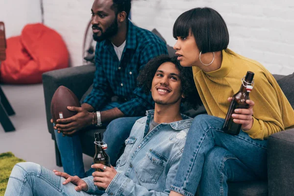 Group of young multiethnic friends with bottles of beer watching american football match — Stock Photo