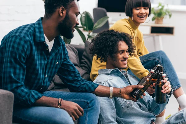 Side view of multiethnic young friends clinking bottles of beer — Stock Photo