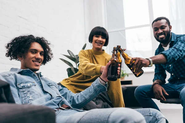 Smiling multicultural young friends clinking bottles of beer — Stock Photo