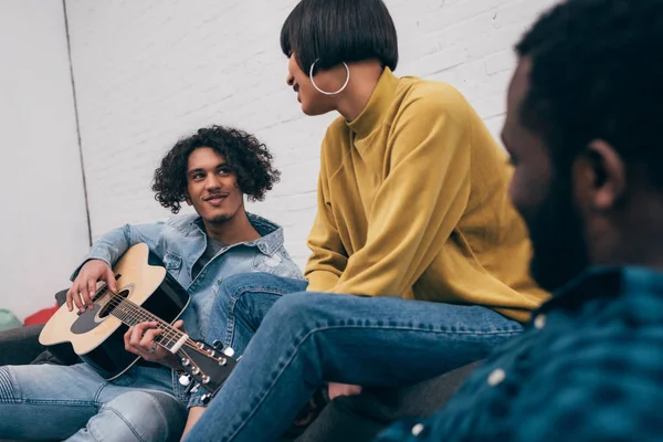 Joven hombre de raza mixta tocando en la guitarra acústica a amigos multiétnicos - foto de stock