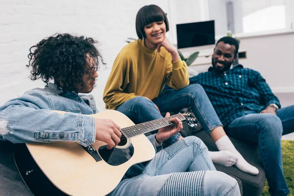 Vue latérale d'un jeune homme métis jouant de la guitare à des amis multiculturels — Photo de stock