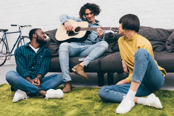 Joven hombre de raza mixta tocando en la guitarra acústica a los amigos - foto de stock