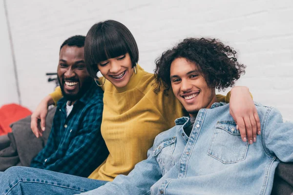 Junge Mischlingsfrau umarmt zwei lächelnde männliche Freunde — Stockfoto