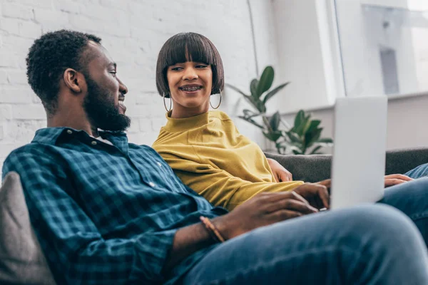 Joven afroamericano hombre utilizando el ordenador portátil y hablando con la novia de raza mixta - foto de stock