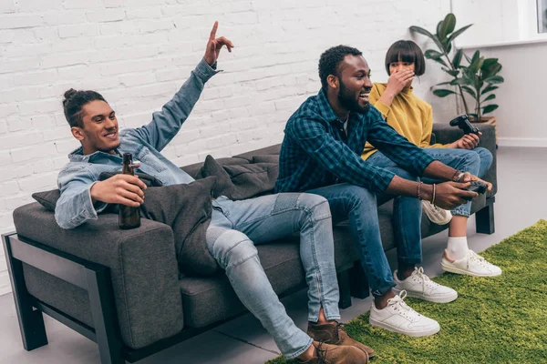 Amigos multiétnicos jugando videojuego y joven de raza mixta con la mano levantada - foto de stock