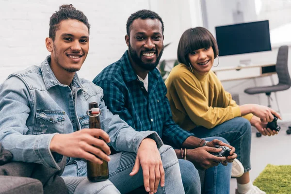 Uomo di razza mista con bottiglia di birra e amici sorridenti con joystick dietro — Foto stock