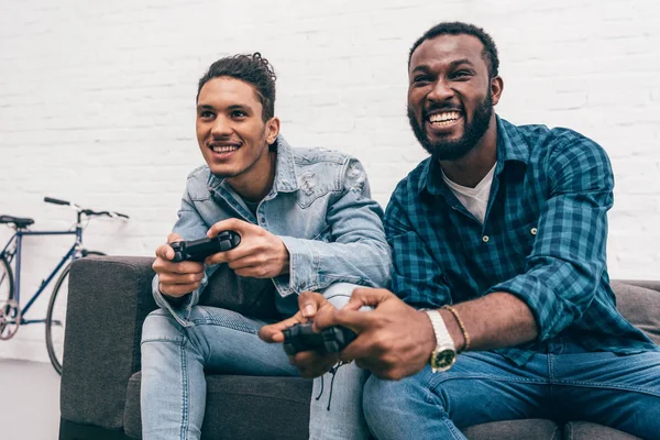 Smiling multicultural young male friends with joysticks playing video game — Stock Photo