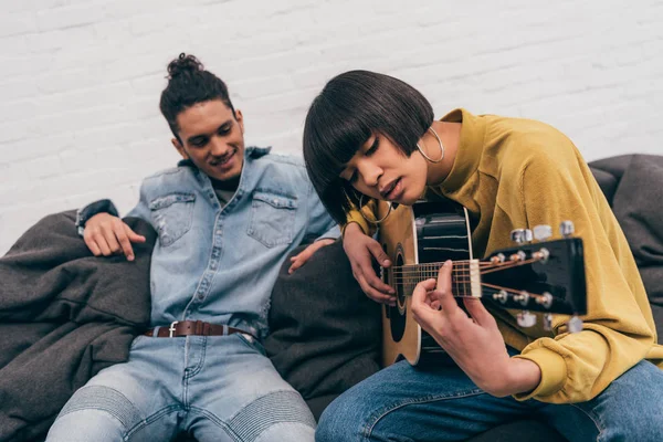 Jovem mulher de raça mista jogando na guitarra acústica para namorado — Fotografia de Stock