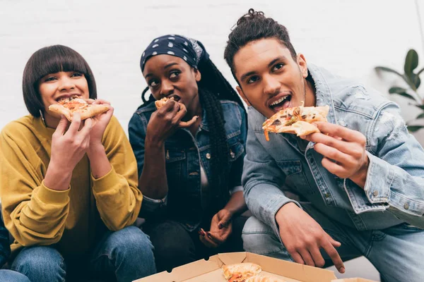 Улыбающаяся мультикультурная группа друзей, которые едят пиццу и смотрят матч — стоковое фото