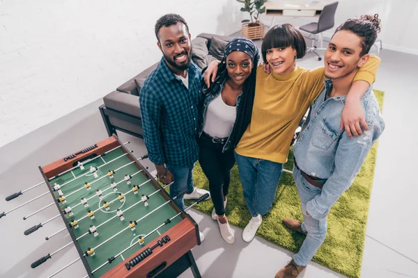 Vista de ángulo alto de amigos multiculturales de pie cerca de tablero de fútbol de mesa - foto de stock