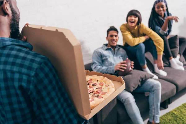Image recadrée de jeune homme noir montrant boîte à pizza à des amis sur le canapé — Photo de stock