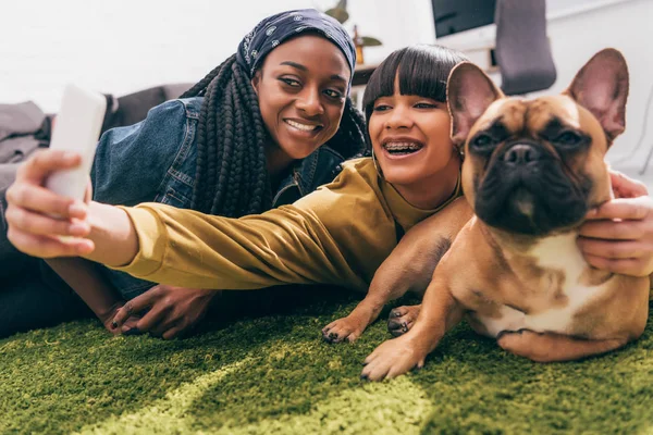 Young multicultural female friends taking selfie with french bulldog — Stock Photo