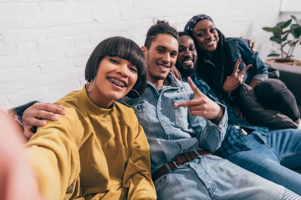 Young mixed race woman taking selfie with multiethnic friends doing peace gesture — Stock Photo