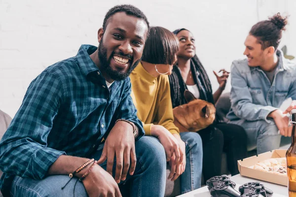 Усміхнений молодий чорний чоловік сидить на дивані з друзями і собакою — Stock Photo