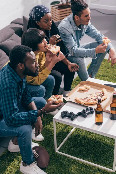 Vista ad alto angolo di amici multietnici mangiare pizza e guardare partita di calcio americano — Foto stock