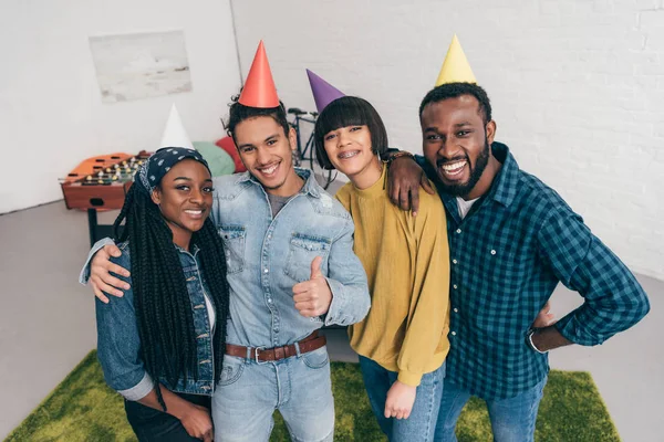 Mixed race young man thumb up standing with friends in party hats — Stock Photo