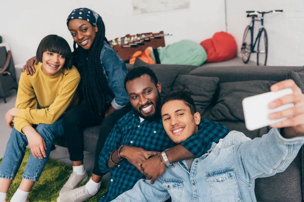 Група молодих мультикультурних усміхнених друзів, які приймають селфі на дивані — стокове фото