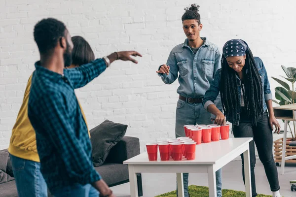 Multiethnic group of friends playing beer pong at table — Stock Photo