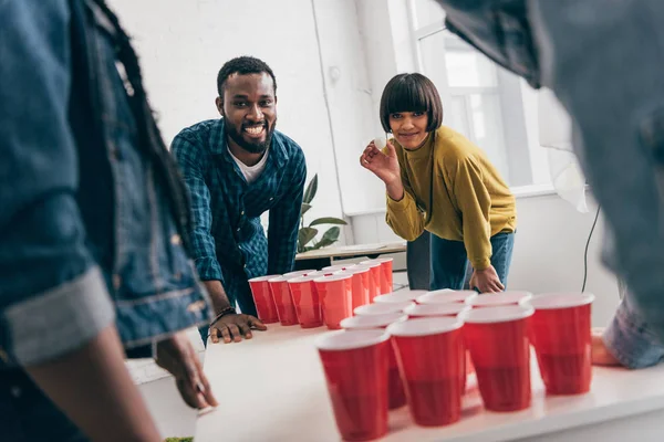 Imagen recortada de grupo multicultural de amigos jugando al pong de cerveza en la mesa - foto de stock