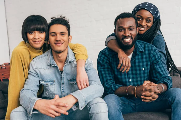 Zwei junge lächelnde Paare, die auf der Couch sitzen und in die Kamera schauen — Stockfoto