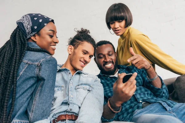 Молодий чорний чоловік вказує на екран смартфона посміхаючись друзям — стокове фото