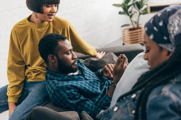 Grupo de amigos multiculturales sentados en el sofá con smartphone - foto de stock