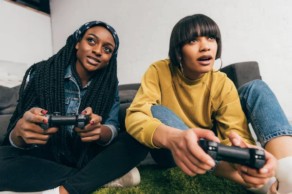 Молодые многонациональные подруги сидят с джойстиками и играют в видеоигры — стоковое фото