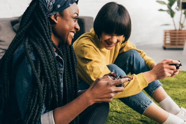 Jóvenes riendo multiétnicos amigos femeninos con joysticks - foto de stock