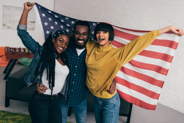 Sonrientes jóvenes amigos multiétnicos de pie con la bandera de EE.UU. - foto de stock