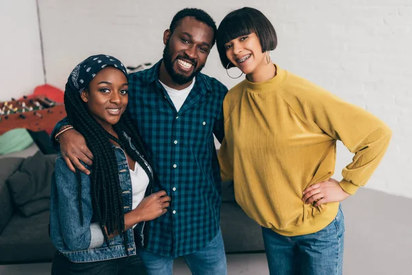 Three multiethnic smiling friends standing and embracing each other — Stock Photo