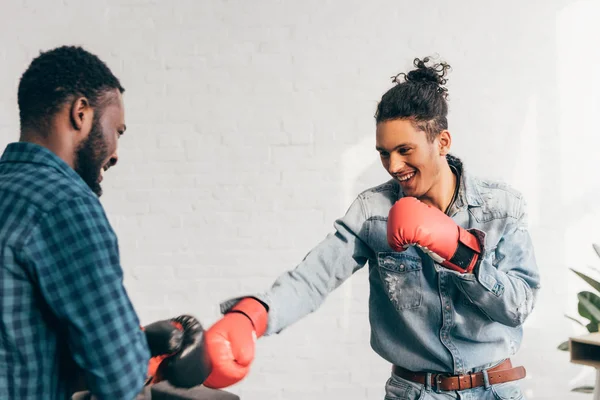 Jóvenes sonrientes amigos masculinos multiétnicos haciendo sparring en guantes de boxeo - foto de stock