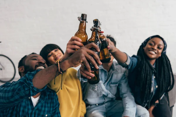 Amigos multiculturales sonrientes tintineando botellas de cerveza - foto de stock