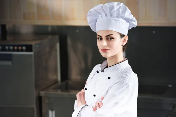 Chef profesional femenino de pie con los brazos cruzados en la cocina moderna - foto de stock